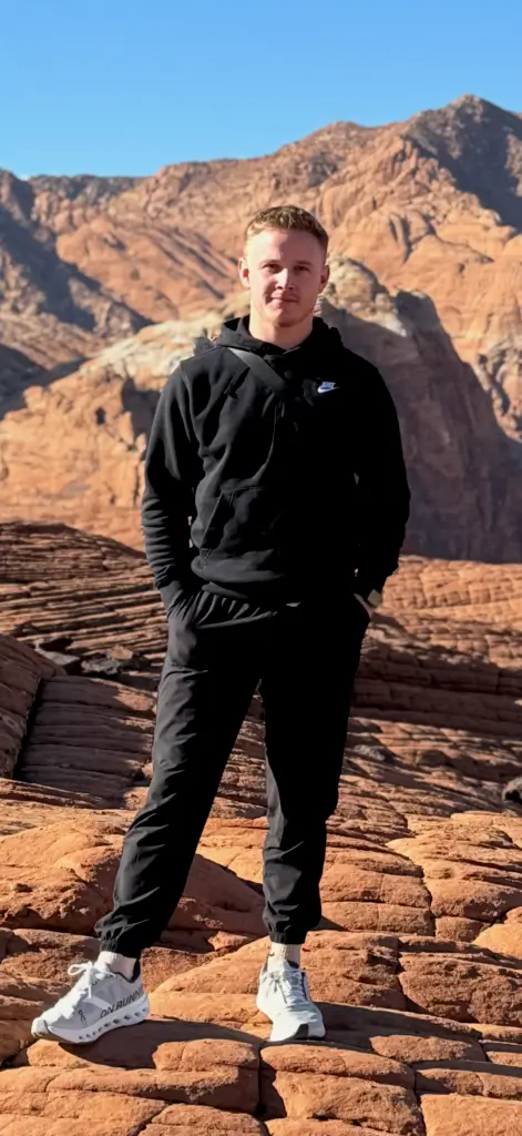 Person in black outfit standing on rocky terrain with canyon background.