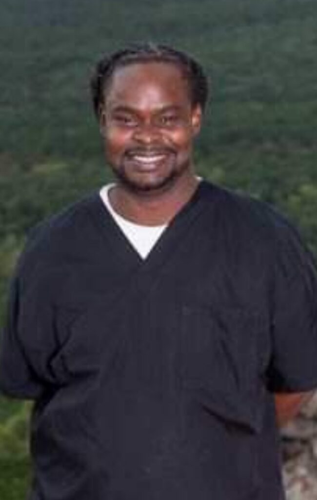 Smiling man in black scrubs outdoors.