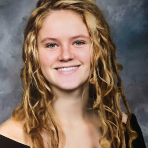 Young woman with curly blonde hair smiling against a dark backdrop.