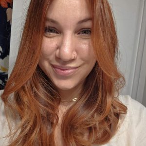 Smiling woman with long, wavy red hair in a casual setting.